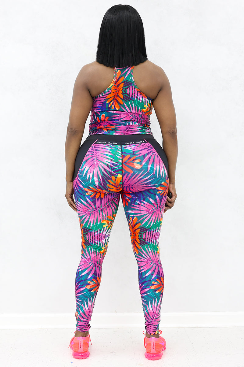 A woman wearing pink floral top with black floral printed tights and pink Nike sports shoes.