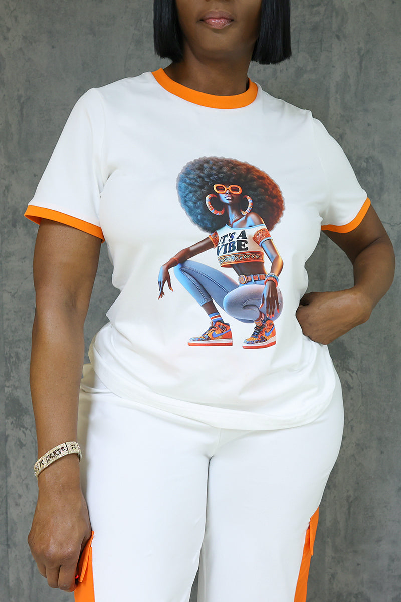 A woman stands against a gray textured background, wearing the Vibe Short Sleeve T-Shirt—white with orange trim and an afro woman print. She pairs it with white pants and poses confidently for a fresh, modern look.