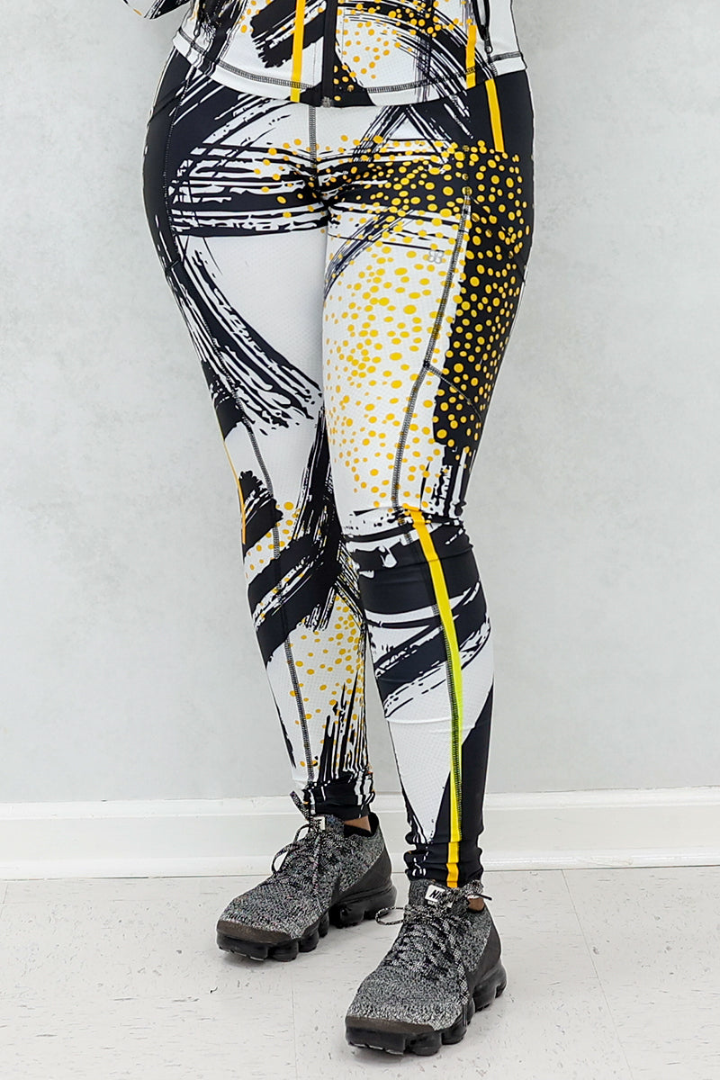 a woman wearing a pair of fitness leggings printed with a black, gold, and white abstract design.