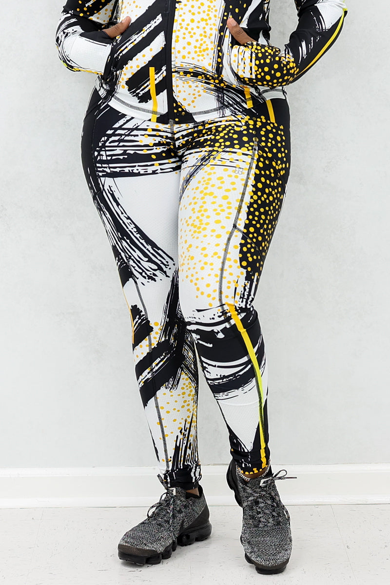 a woman wearing a pair of fitness leggings printed with a black, gold, and white abstract design.