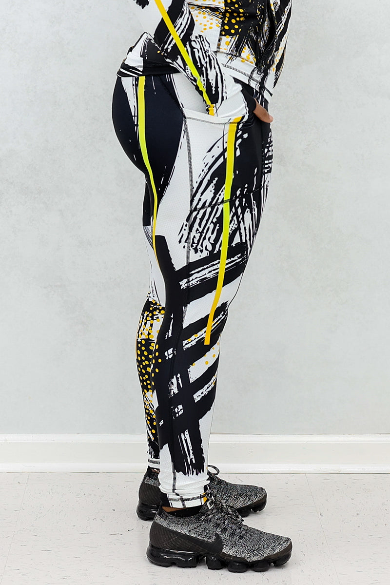 a woman wearing a pair of fitness leggings printed with a black, gold, and white abstract design.