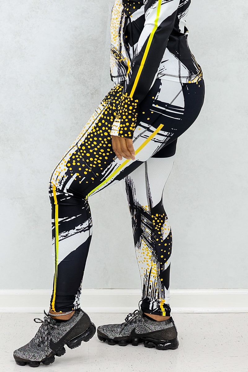 a woman wearing a pair of fitness leggings printed with a black, gold, and white abstract design.