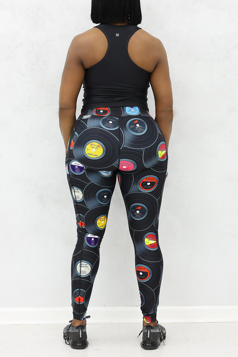 A woman wearing black tank top and tights with vinyl record print and black sneakers.