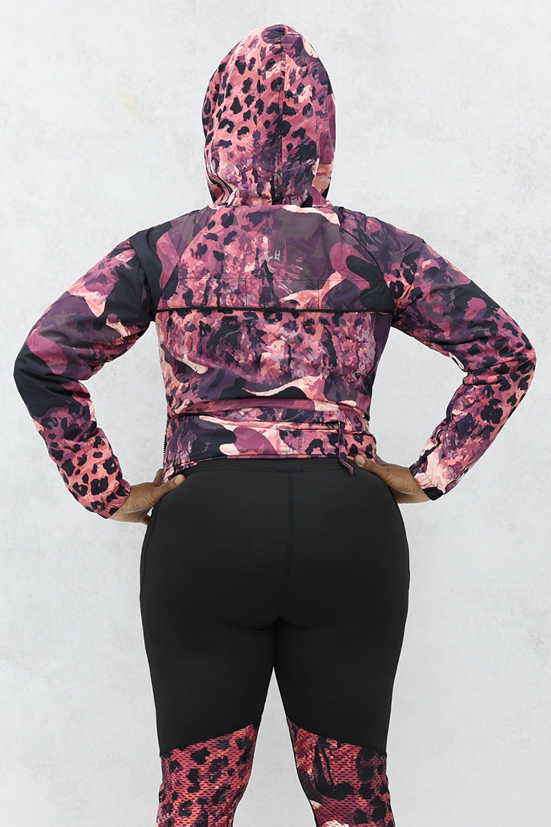 A woman wearing a black and pink Graphic Pouch jacket, a packable windbreaker with a hood and multiple pockets.