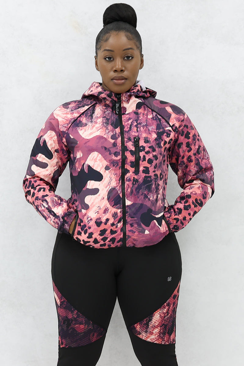 A woman wearing a black and pink Graphic Pouch jacket, a packable windbreaker with a hood and multiple pockets.