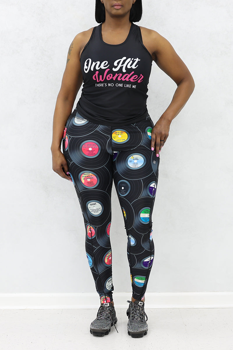 A woman wearing black tank top and tights with vinyl record print, and black sneakers.