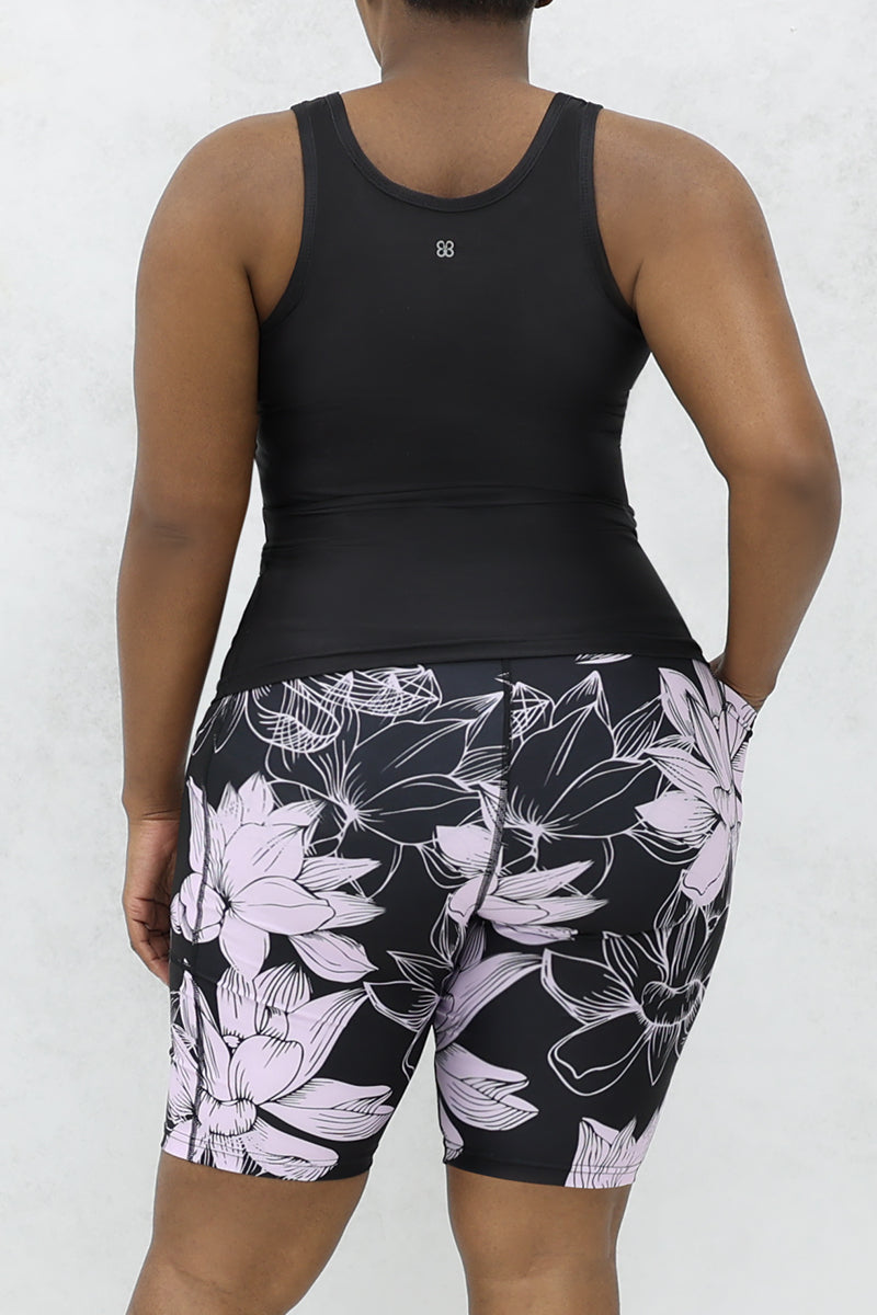 A woman wearing a tank top and floral lavender and black tights, playfully expressing "protecting my peach with these tights." The stylish shorts feature a bold floral pattern, adding flair to her outfit and making it a versatile addition to her wardrobe.