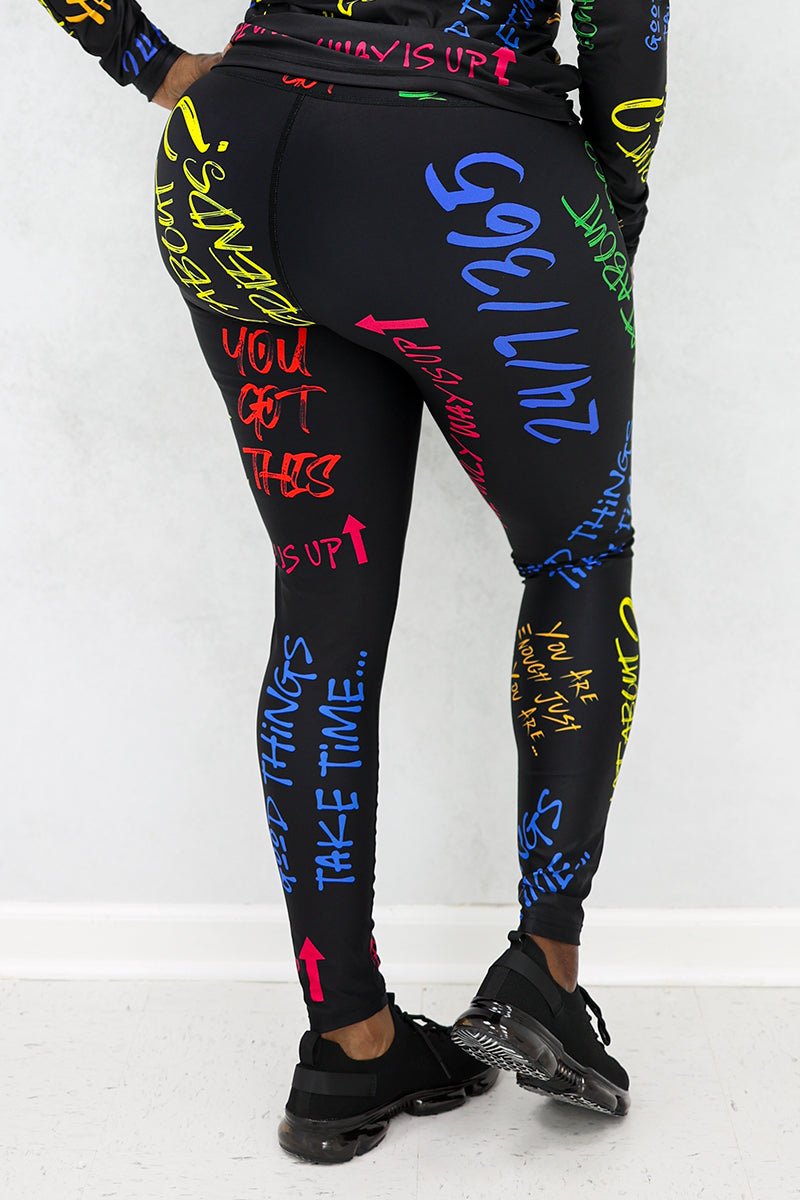 A woman wearing Quote Tights in black with multi-colored inspiring quotes, designed with durable, stretchy fabric and a continuous drawstring for comfort during workouts.