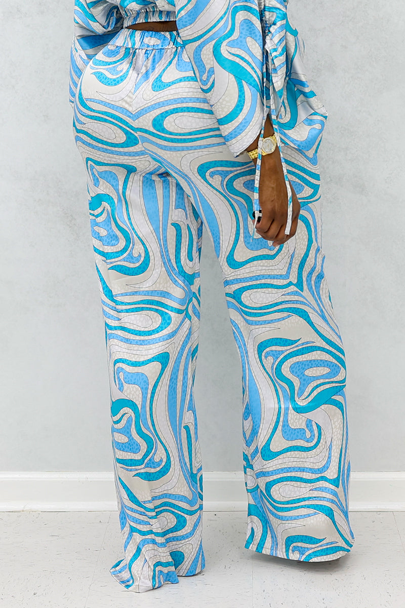 A woman wearing multi-colored Satin Darling Pants featuring a flared design, elastic waistband, front zipper, and pockets, offering a trendy and cozy silky smooth experience.
