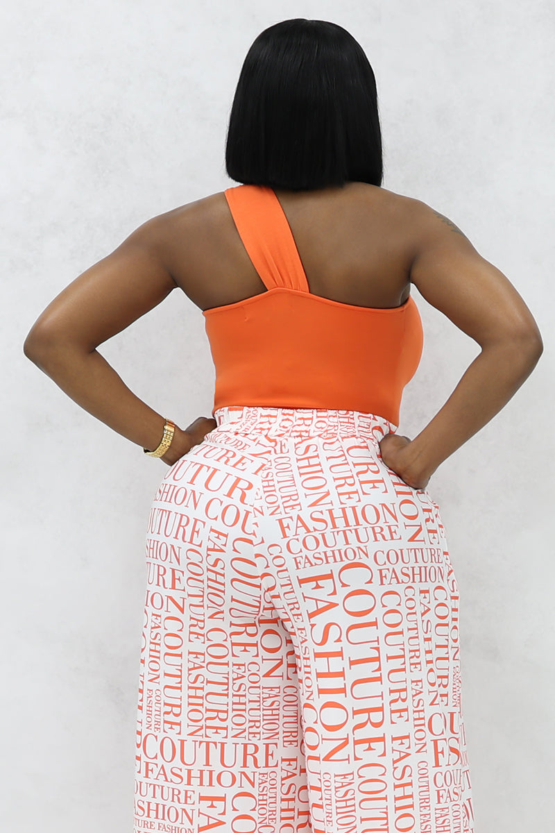 A woman wearing orange sunglasses with an orange colored twisted tank top and white Couture Fashion pants.