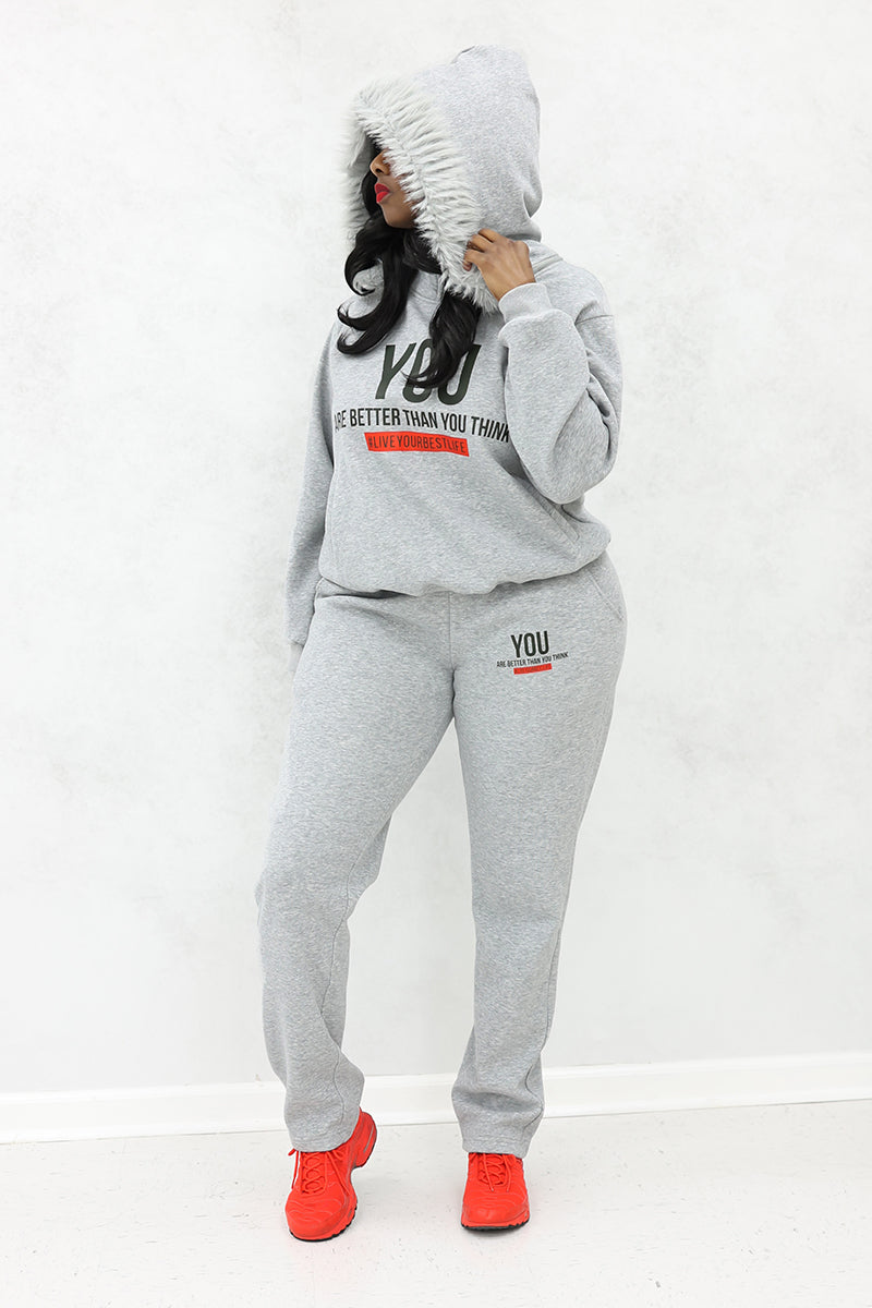 A woman wearing white fur-lined hood, "YOU" Fur hoodie, joggers with pockets and red shoes.