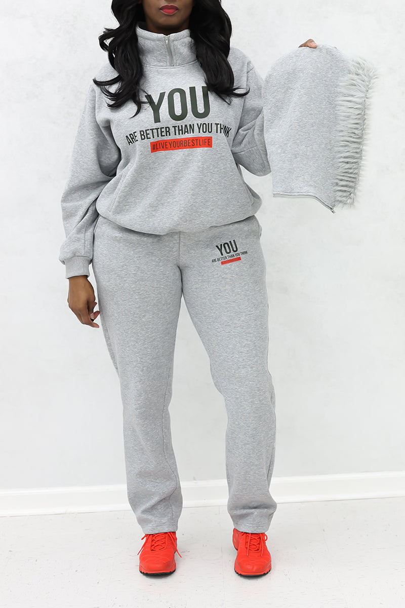 A woman holding a fur throw, wearing a "YOU" Fur hoodie and joggers along with red shoes.
