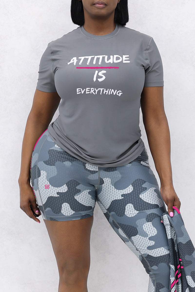 Donning an Attitude Is Everything gray t-shirt and camo shorts, this individual epitomizes casual comfort. The relaxed fit, made from soft and lightweight fabric, stands out against the white backdrop while they hold another piece of clothing.
