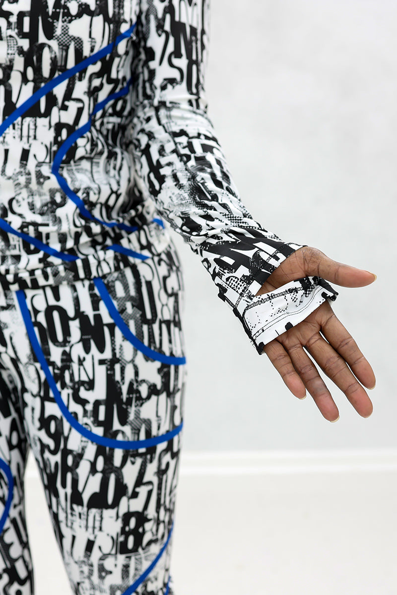 Wearing the Blue Streak 1/2 Zip Pullover with a black and white abstract pattern and blue accents, the person extends their left arm to display thumbhole sleeves against a plain light background.