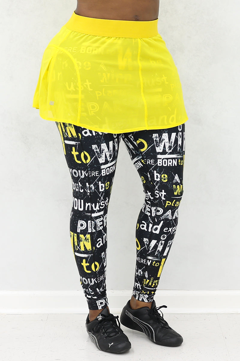 A woman wearing a yellow mesh tennis skirt with printed black tights. The skirt features a stretchy material and a drawstring waist for comfort and style.
