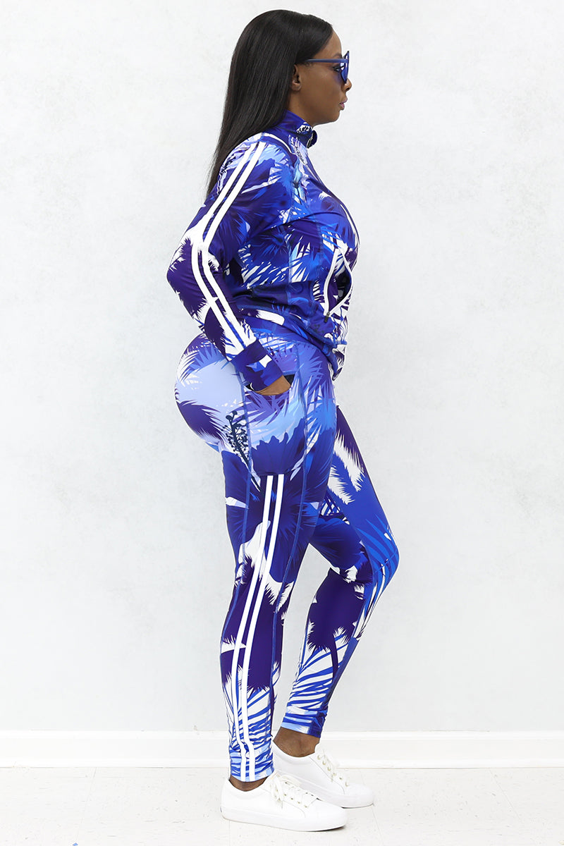 A woman wearing blue and white tropical printed jacket and tights with pockets and white shoes