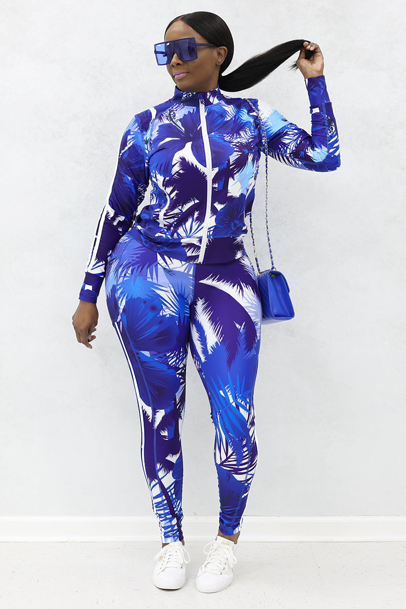 A woman wearing blue and white tropical-printed jacket with tights, white shoes, blue purse and blue sunglasses.