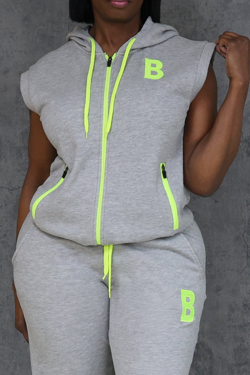 A person in a Gray-Green Sleeveless Hoodie with neon yellow accents, color-block design, and letter B on the chest and thigh stands against a gray textured wall.