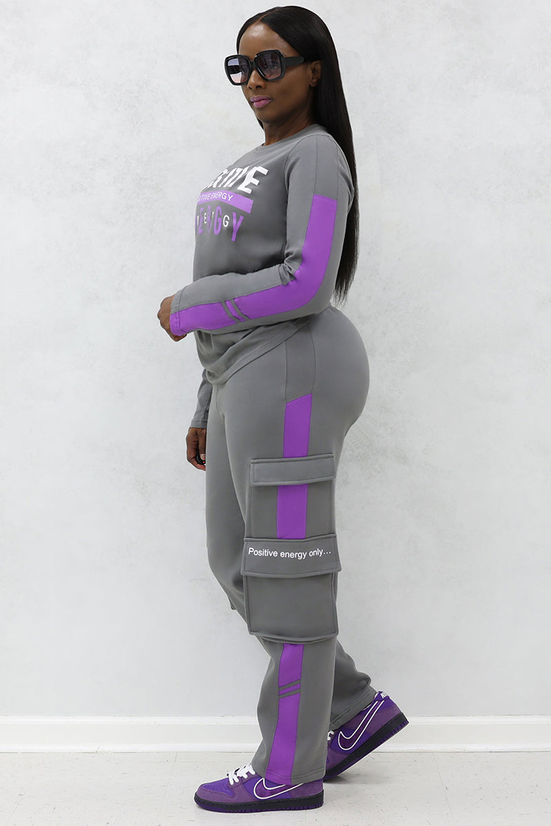A woman wearing black glasses, gray and purple cargo tracksuit with pockets and purple Nike shoes