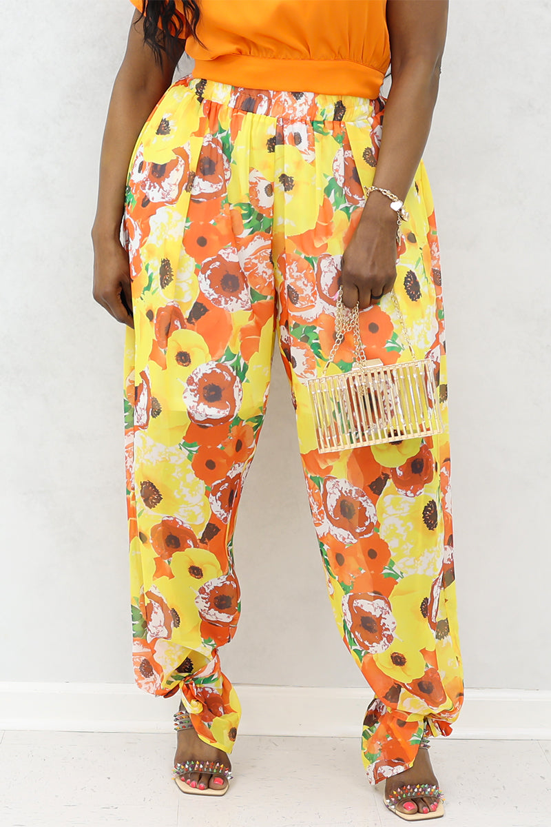 A woman wearing yellow and orange floral poppies tie ankle pants with heels and a purse.