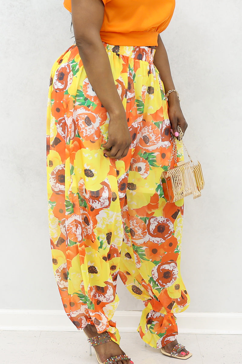 A woman wearing yellow and orange floral poppies tie ankle pants with heels and a purse.