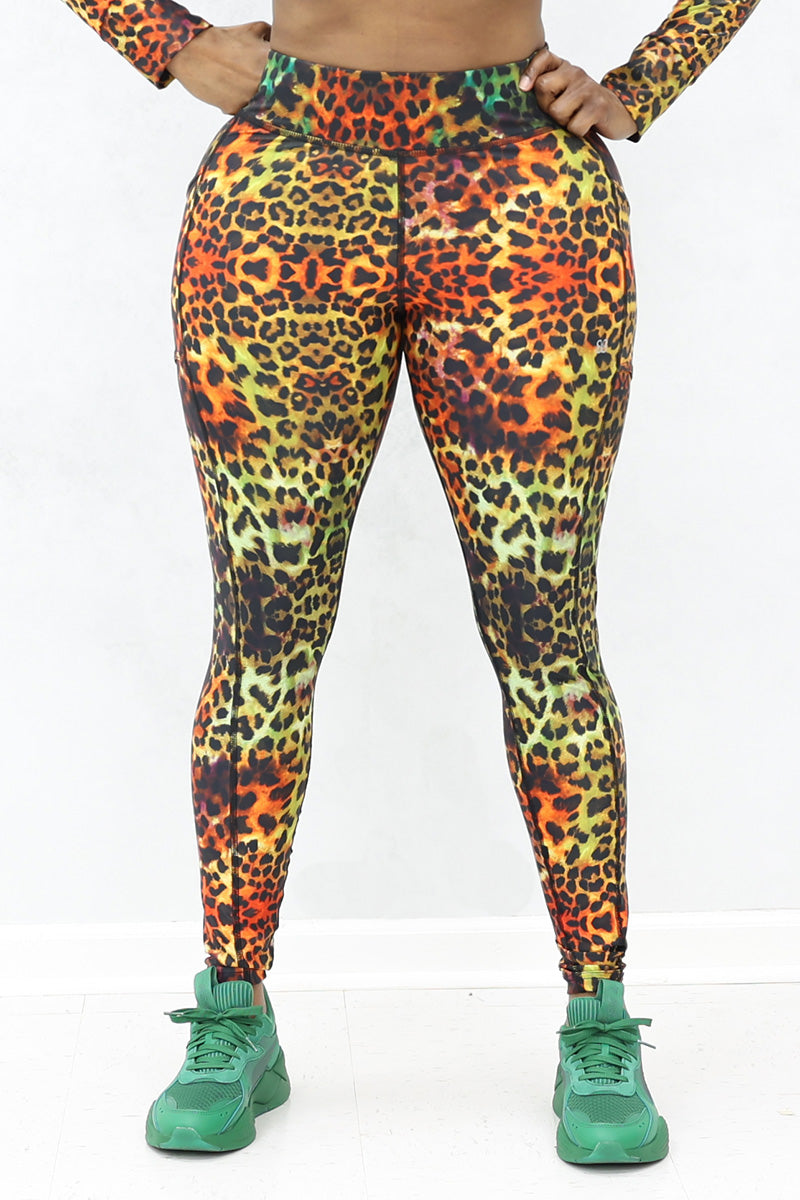 A person wearing high-waisted, tight-fitting Safari Tights in a multi-colored print stands against a plain white background, paired with green athletic shoes.