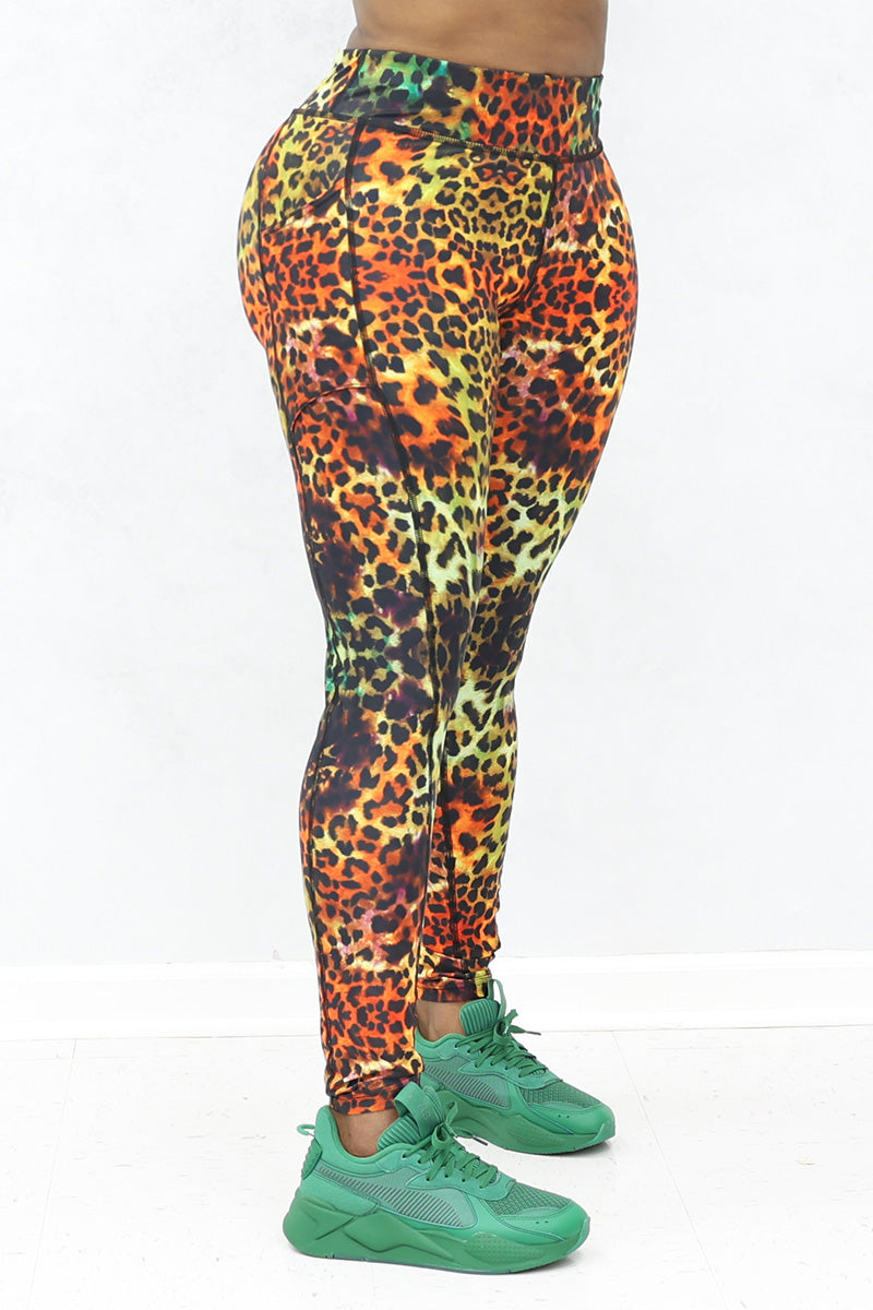 A person models high-waisted Safari Tights featuring an orange and yellow cheetah print and stretchy fabric, paired with green athletic shoes. Only the lower body is visible against a plain white background.