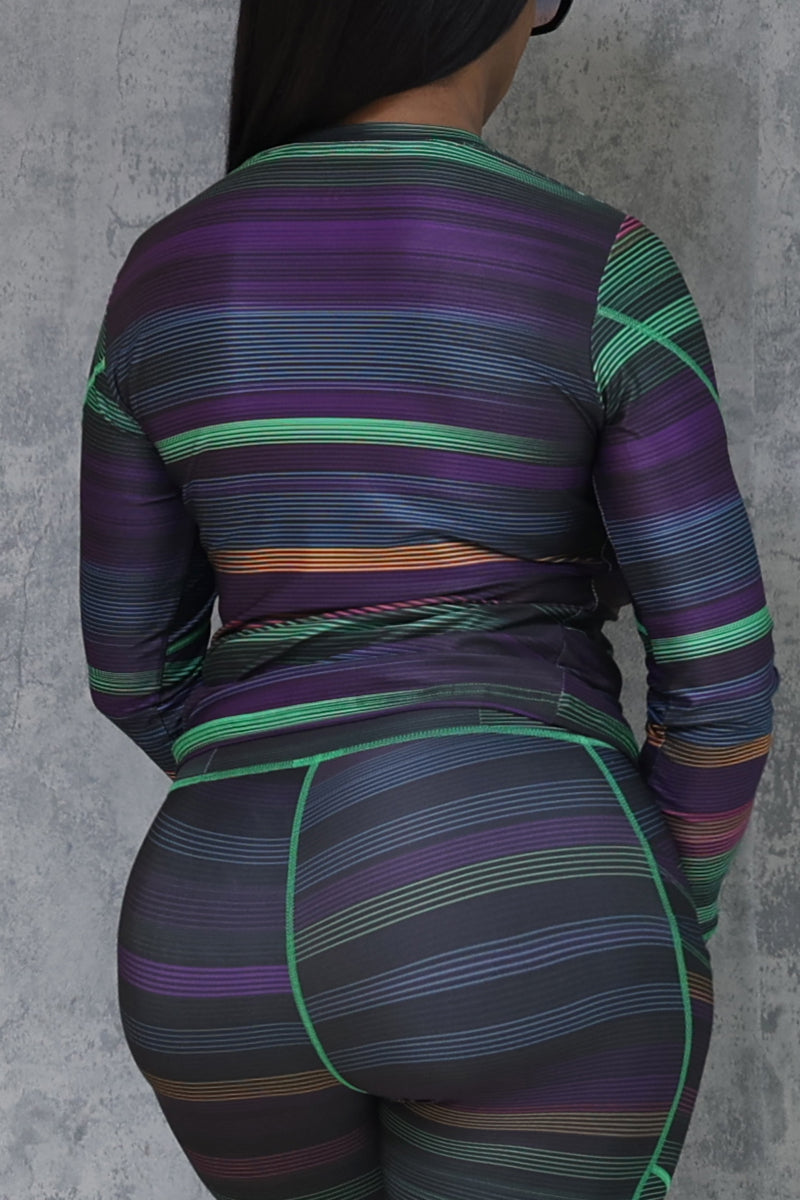 A person faces away from the camera, wearing the Sidelines Long Sleeve T-Shirt—a form-fitting, moisture-wicking top with horizontal green, purple, and orange stripes on a dark background—against a light gray textured wall.