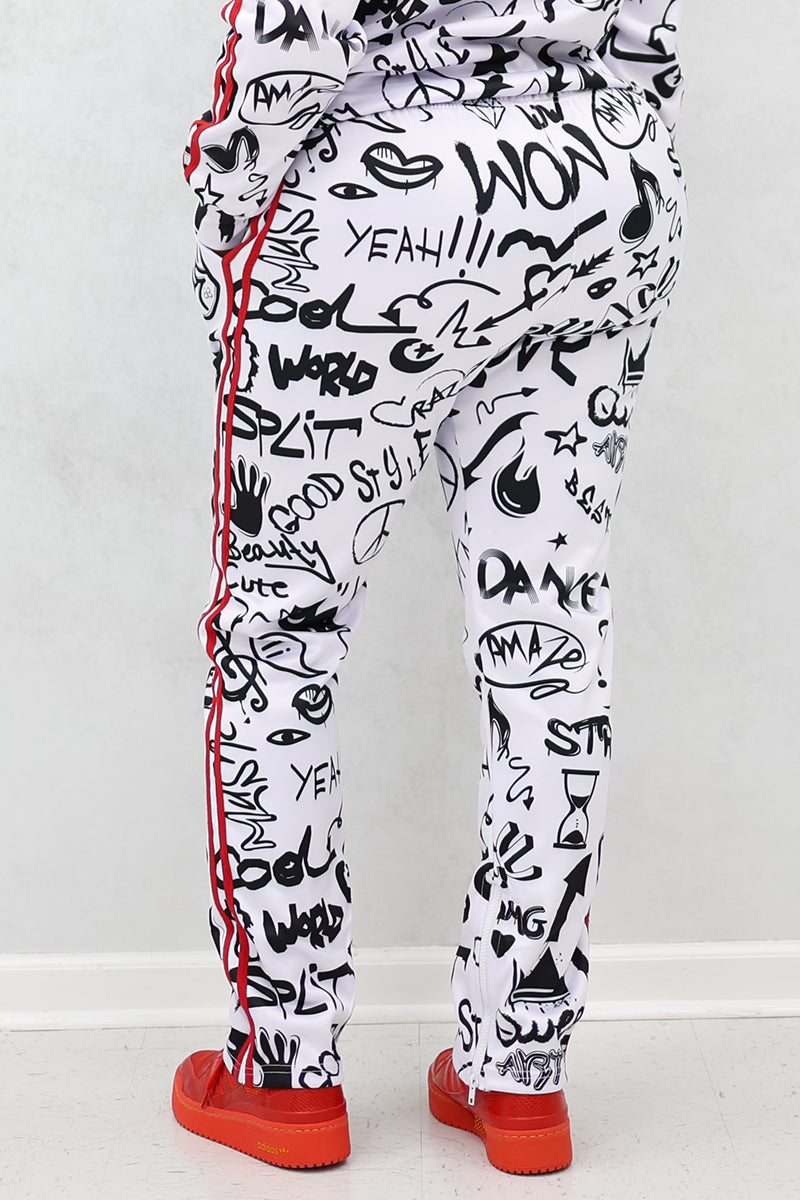 A person faces away from the camera, wearing Street Sweatpants with a relaxed fit, black graffiti-style text and drawings, red side stripes, and red shoes. The background features a plain light-colored wall and floor.