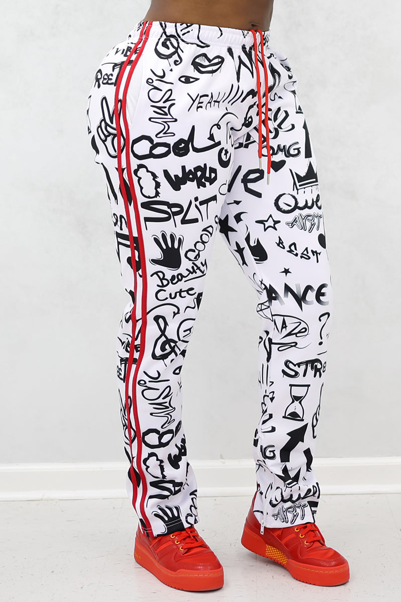 Someone stands on a white floor against a light background, wearing Black-White Street Sweatpants featuring relaxed fit, black graffiti-style text and drawings, red side stripes, and red sneakers.