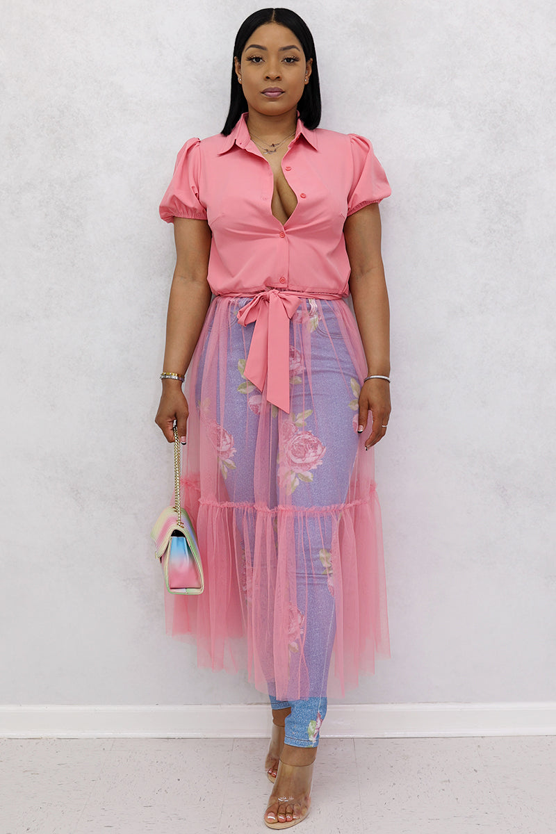 A woman wearing pink mesh top, floral tulle skirt, jeans, clear heels and a purse.