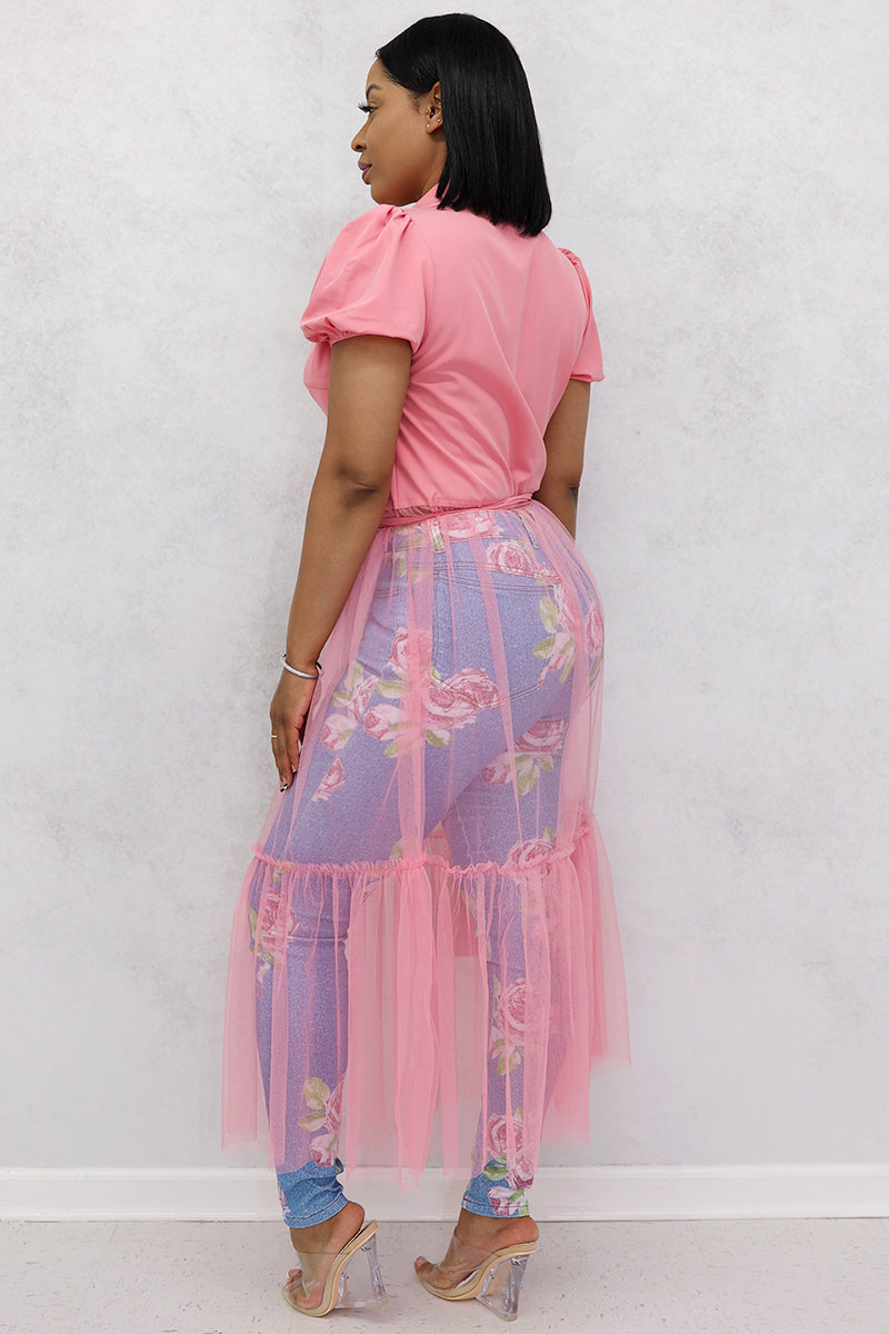 A woman wearing pink mesh top, floral tulle skirt, jeans, and clear heels.
