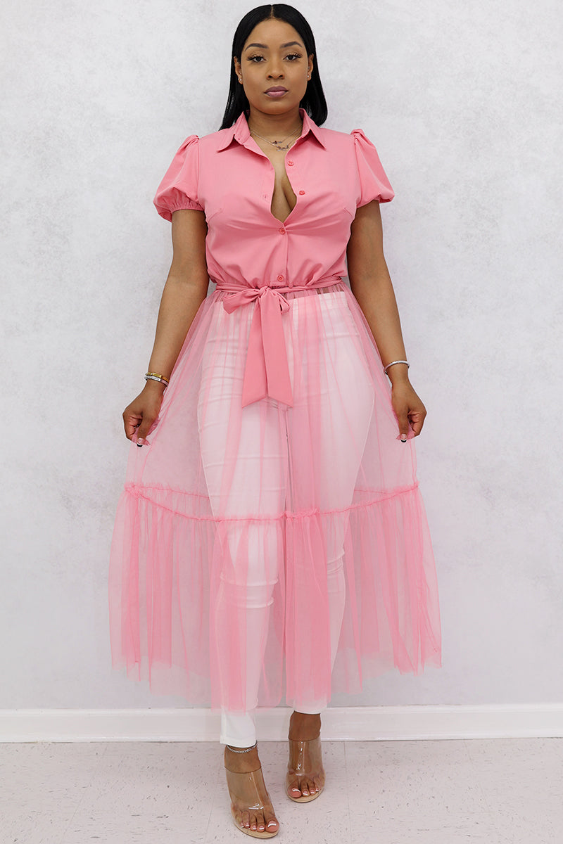 A woman wearing pink mesh top, floral tulle skirt, white jeans, clear heels, and a purse.