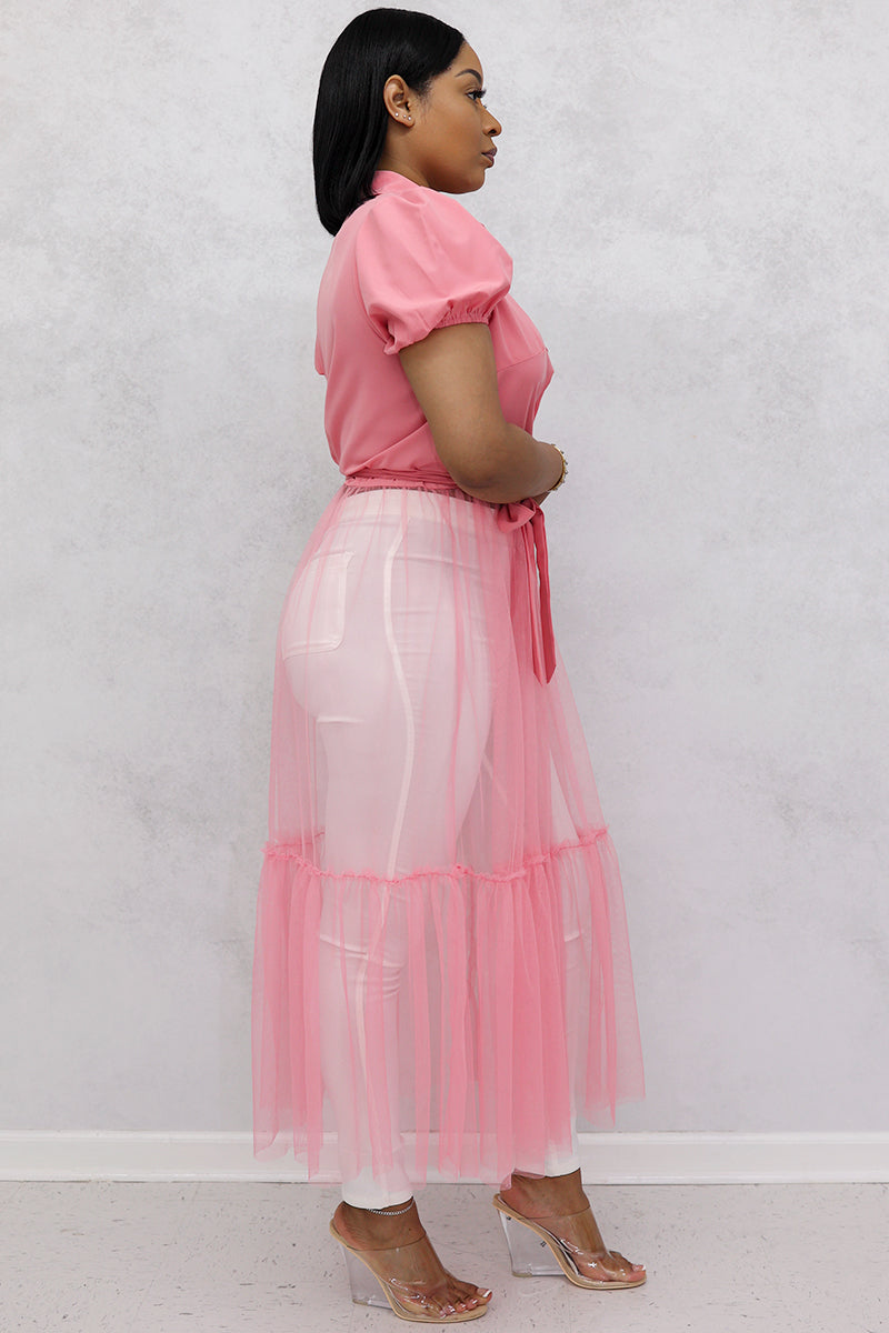 A woman wearing pink mesh top, floral tulle skirt, white jeans, and clear heels.
