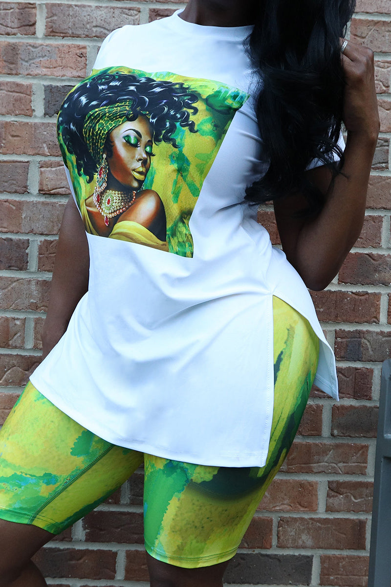 A woman wearing a white T-shirt with a black woman's image printed in a square and green shorts is standing against a brick wall.