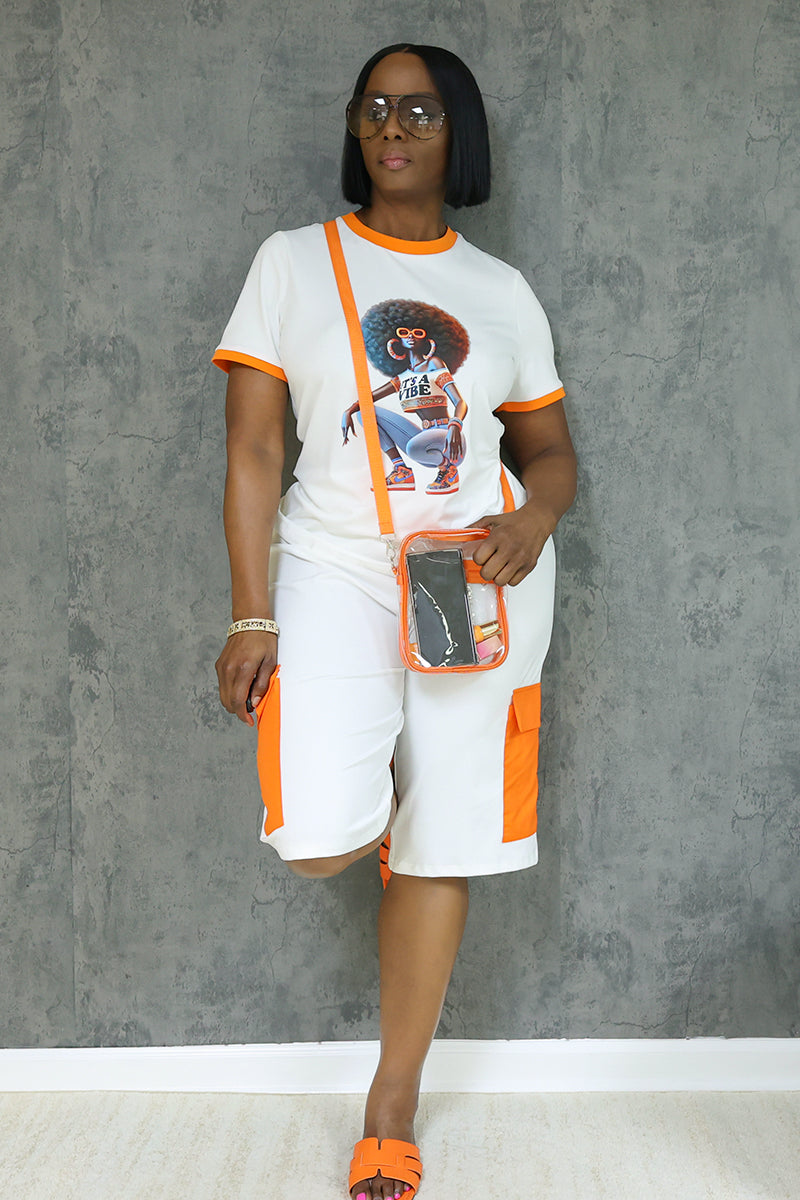 A woman stands against a gray wall wearing the Vibe Short Sleeve T-Shirt with an afro woman graphic, orange-accented lightweight outfit, orange sandals, glasses, and a clear crossbody bag.