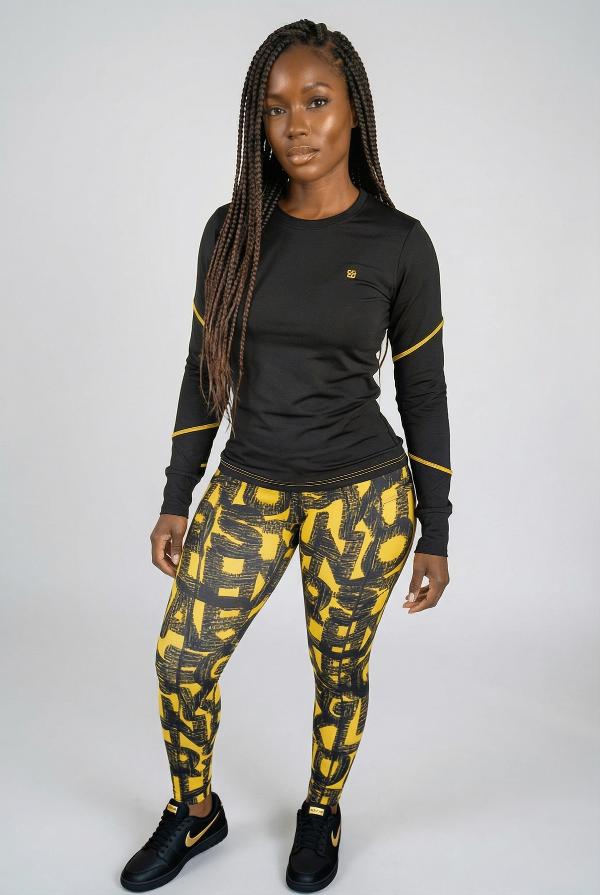 A woman stands against a light background, wearing Black & Yellow Tights—a long-sleeve black athletic top with yellow accents and matching stretchy leggings of lightweight, breathable fabric—paired with black athletic shoes featuring yellow details.