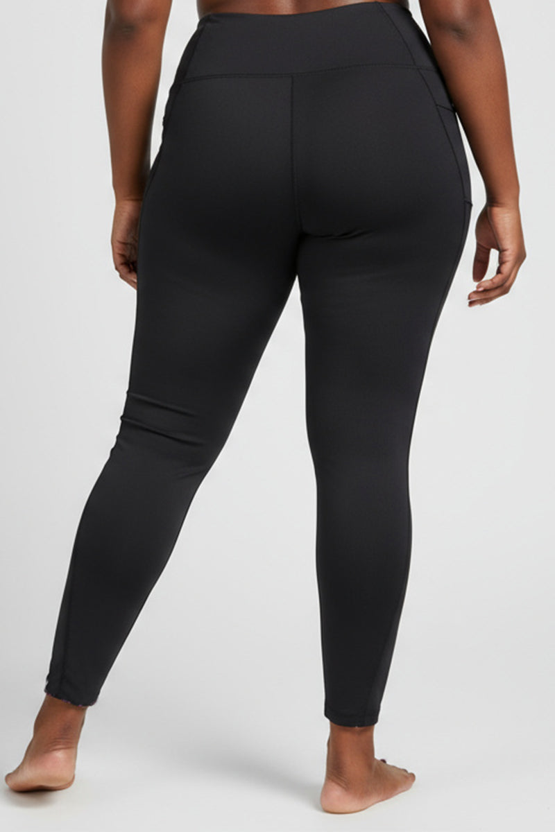 A person stands barefoot, facing away from the camera, wearing high-waisted black Hope Tights (SAMPLE) against a plain light background.