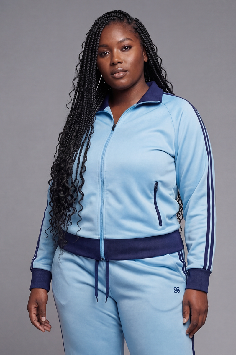 Woman wearing a light blue tracksuit with dark blue accents on a gray background
