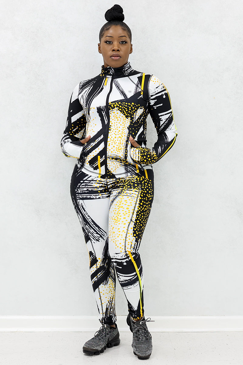 a woman wearing a fitted fitness jacket printed with a black, gold, and white abstract design. 