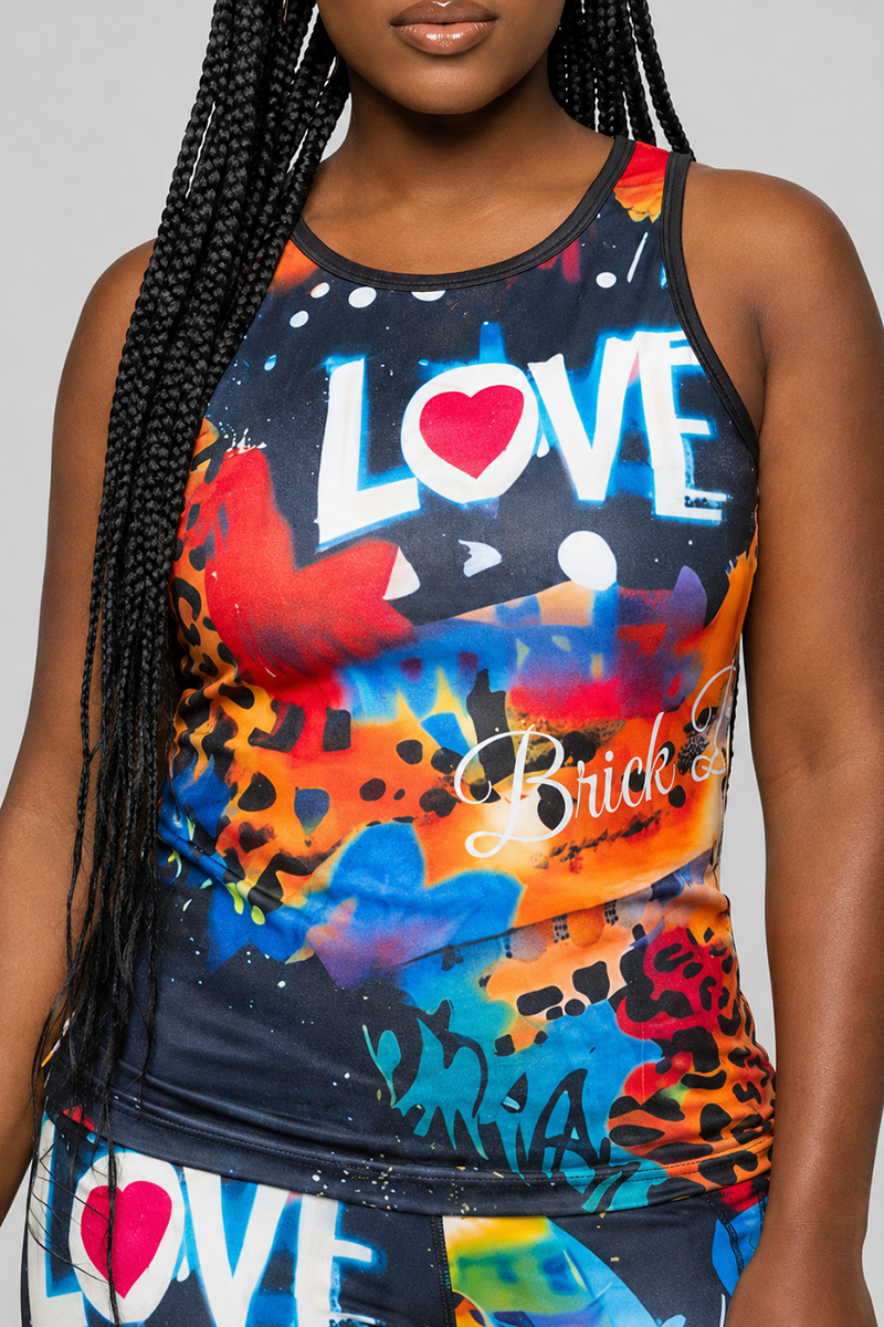A woman with long braids wears the Art Code Tank Top in Multi, a colorful and lightweight racerback featuring the words LOVE and Brick among abstract, graffiti-style designs in blue, red, orange, and white. Only her upper body and clothing are visible.