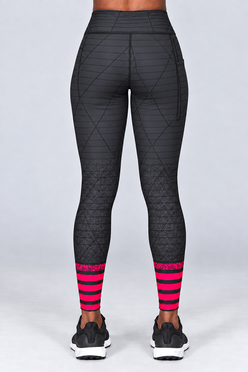 Wearing the Epic Tights—gray-black leggings featuring a diamond pattern and a body contouring fit—a person with black shoes and pink striped accents near the ankles stands facing away from the camera against a plain light background.
