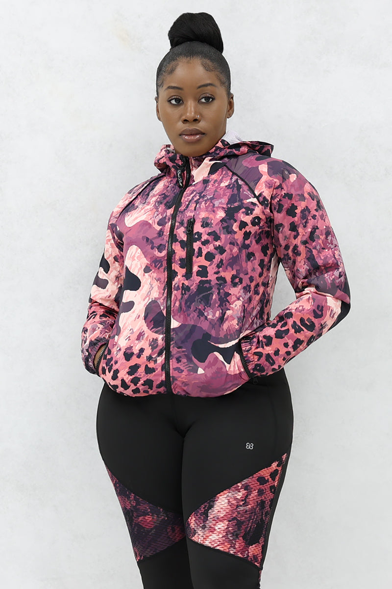 A woman wearing a black and pink Graphic Pouch jacket, a packable windbreaker with a hood and multiple pockets.