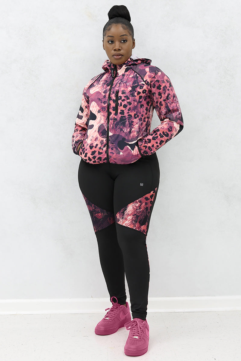 A woman wearing a black and pink Graphic Pouch jacket, a packable windbreaker with a hood and multiple pockets.