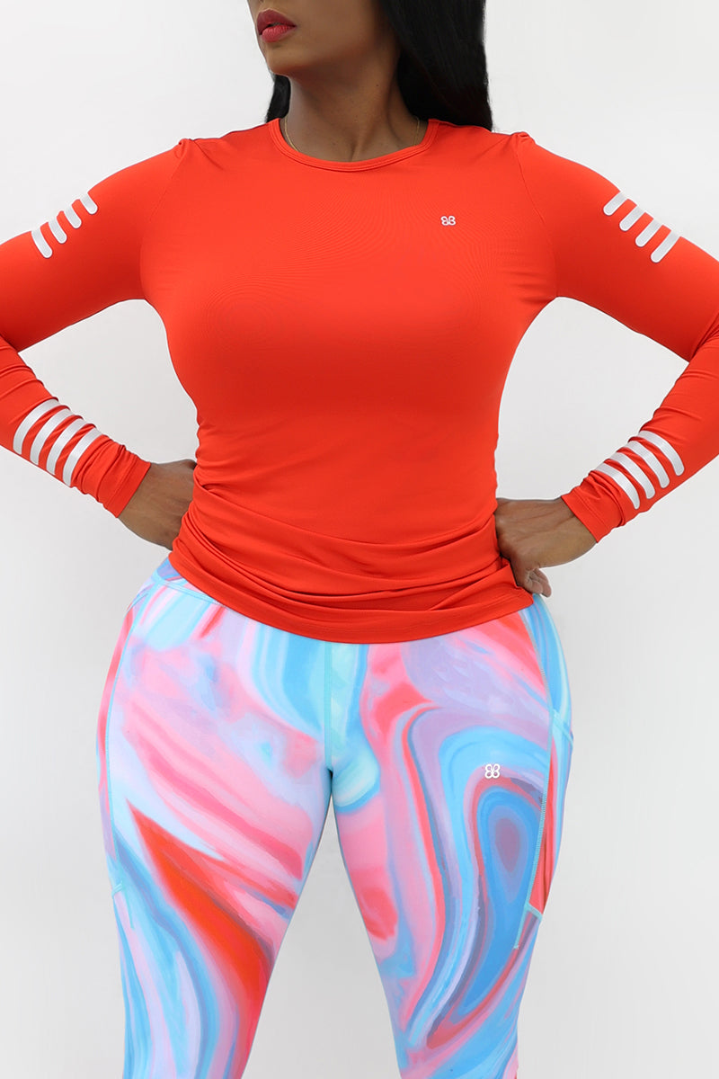  A woman wearing an orange long sleeve training t-shirt with reflective stripes on the shoulders and arms, designed for an active lifestyle. 