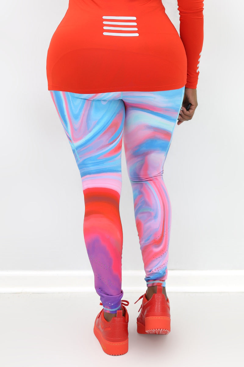 A woman wearing marbled tights in vibrant colors, featuring a drawstring waistband and laser perforations at the ankles. The tights have deep side pockets and a zippered pocket on the back, showcasing a blend of comfort and style ideal for workouts or everyday wear.