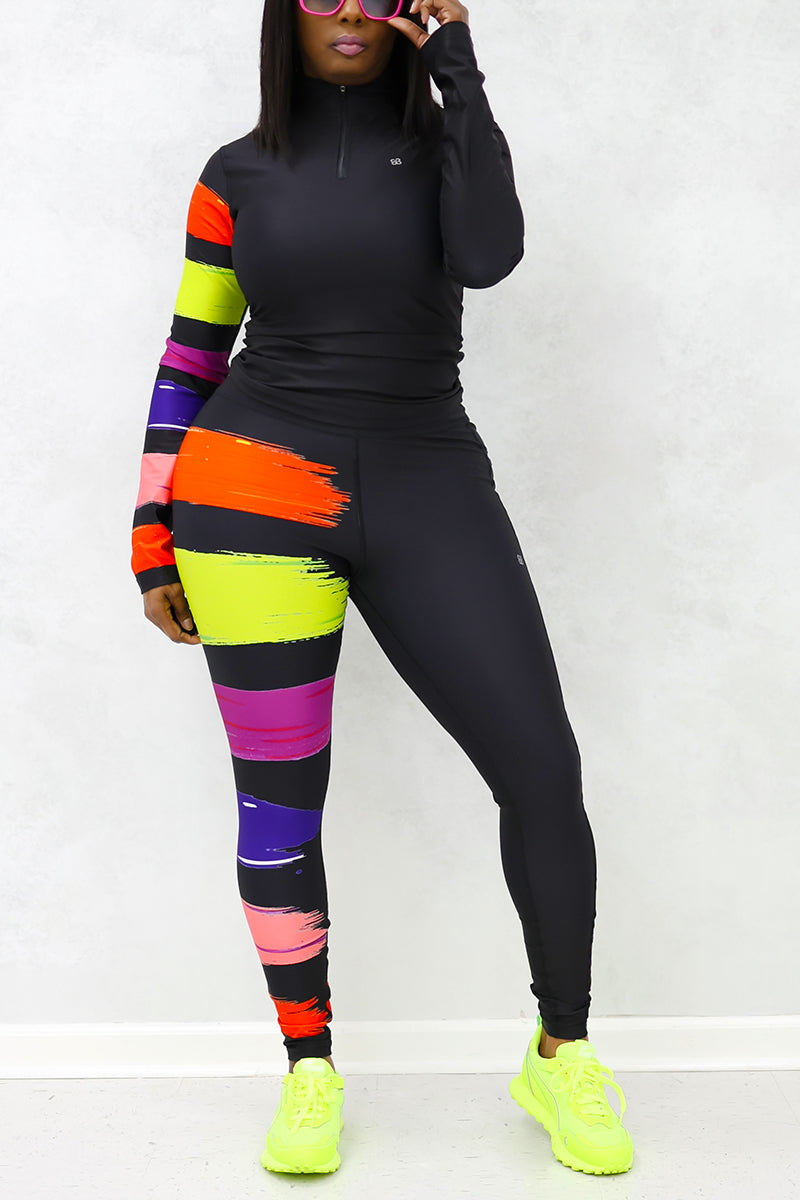 A woman wearing the Paint Strokes Half-Zip Pullover in vibrant multi colors, featuring a half zipper and a pocket on the left leg, showcasing a stylish blend of black, orange, lime, and purple.