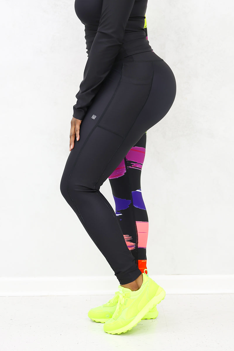 A woman wearing the Paint Strokes Tights in a vibrant multi-color design, featuring a pocket on the left thigh and a continuous drawstring, perfect for adding creativity to her workout routine.