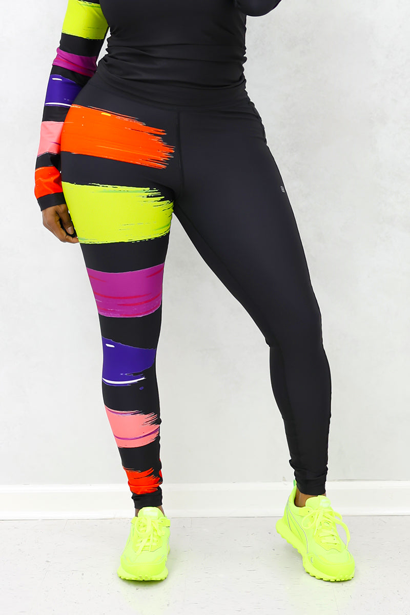 A woman wearing the Paint Strokes Tights in a vibrant multi-color design, featuring a pocket on the left thigh and a continuous drawstring, perfect for adding creativity to her workout routine.