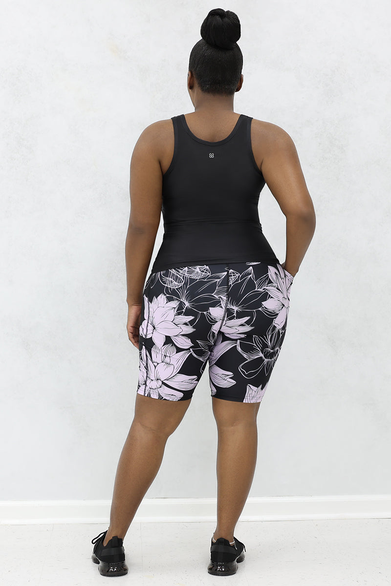 a woman wearing a black 
tank top with 'Protecting My Peace,' printed on the front 
paired with black and lavender floral printed shorts